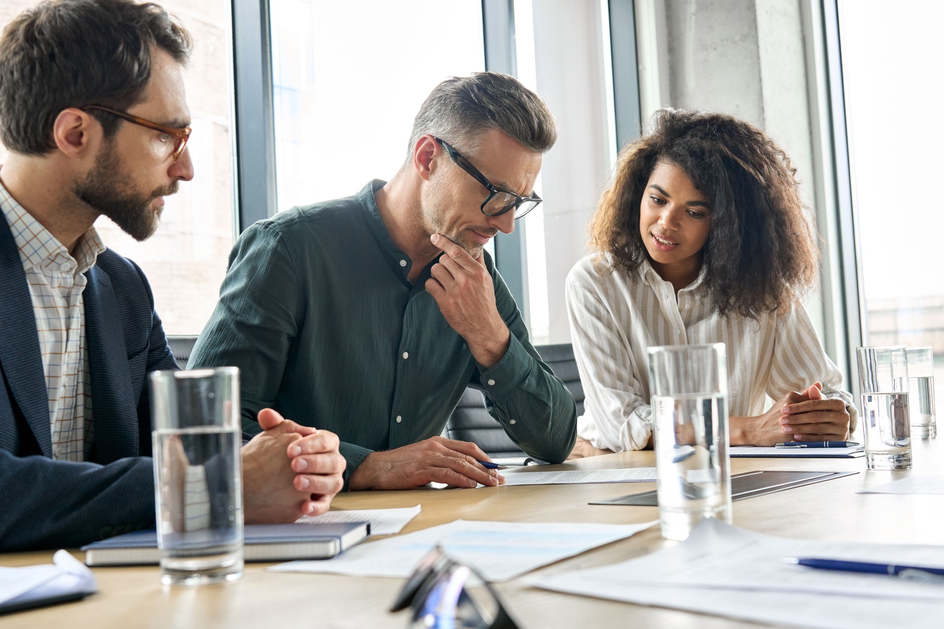 Focused mature businessman reading contract considering risks with lawyers.